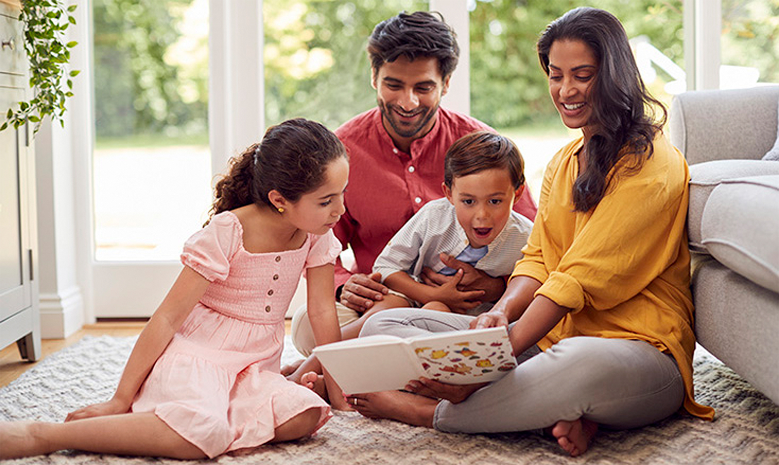 Family reading a book together on the living room floor